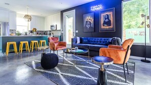 A modern kitchen with a bar area, a blue sofa, and orange chairs in a living room with a black and white rug. - Electric Disco Oasis Near Rainey, UT and Top Spots (Austin)