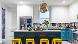A modern kitchen with a central island, stainless steel appliances, and yellow stools. - Electric Disco Oasis Near Rainey, UT and Top Spots (Austin)