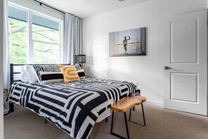Un dormitorio moderno con una cama grande, un banco, una ventana con cortinas y una puerta.