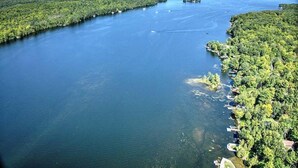 An aerial view of a river with dense forested areas on both sides, boats docked along the right bank, and a clear sky. - Pet Friendly Home Near Lock 32 & Beach Park (Kawartha Lakes)