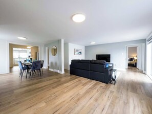 A modern living room with a black sofa, a dining area with chairs, and a kitchen in the background.
