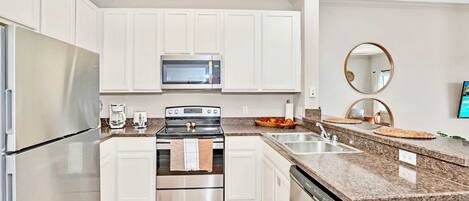 A modern kitchen with white cabinets, stainless steel appliances, granite countertops, and a built-in oven.