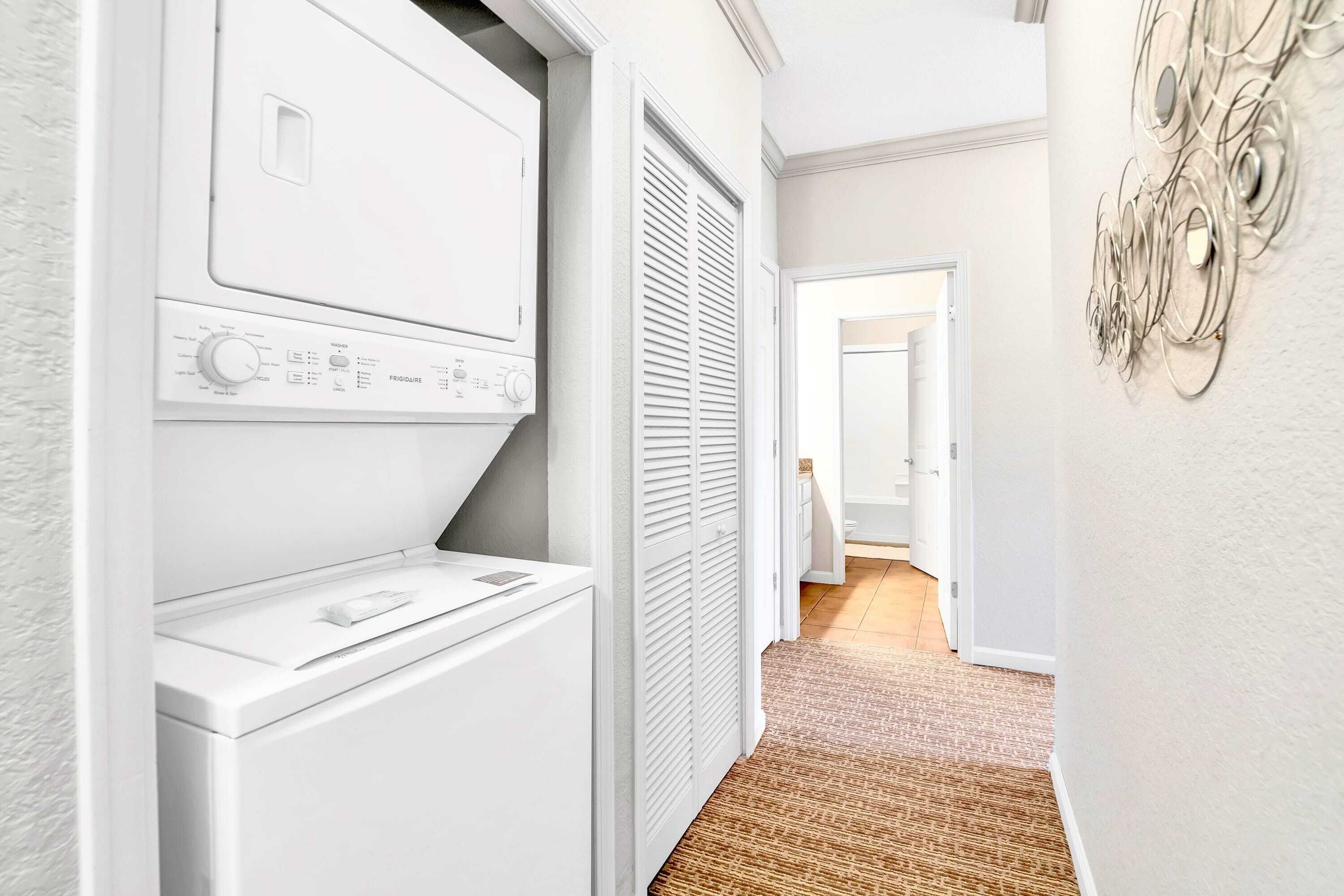 A laundry room with a washer and dryer, a door leading to another room, and a textured carpet.