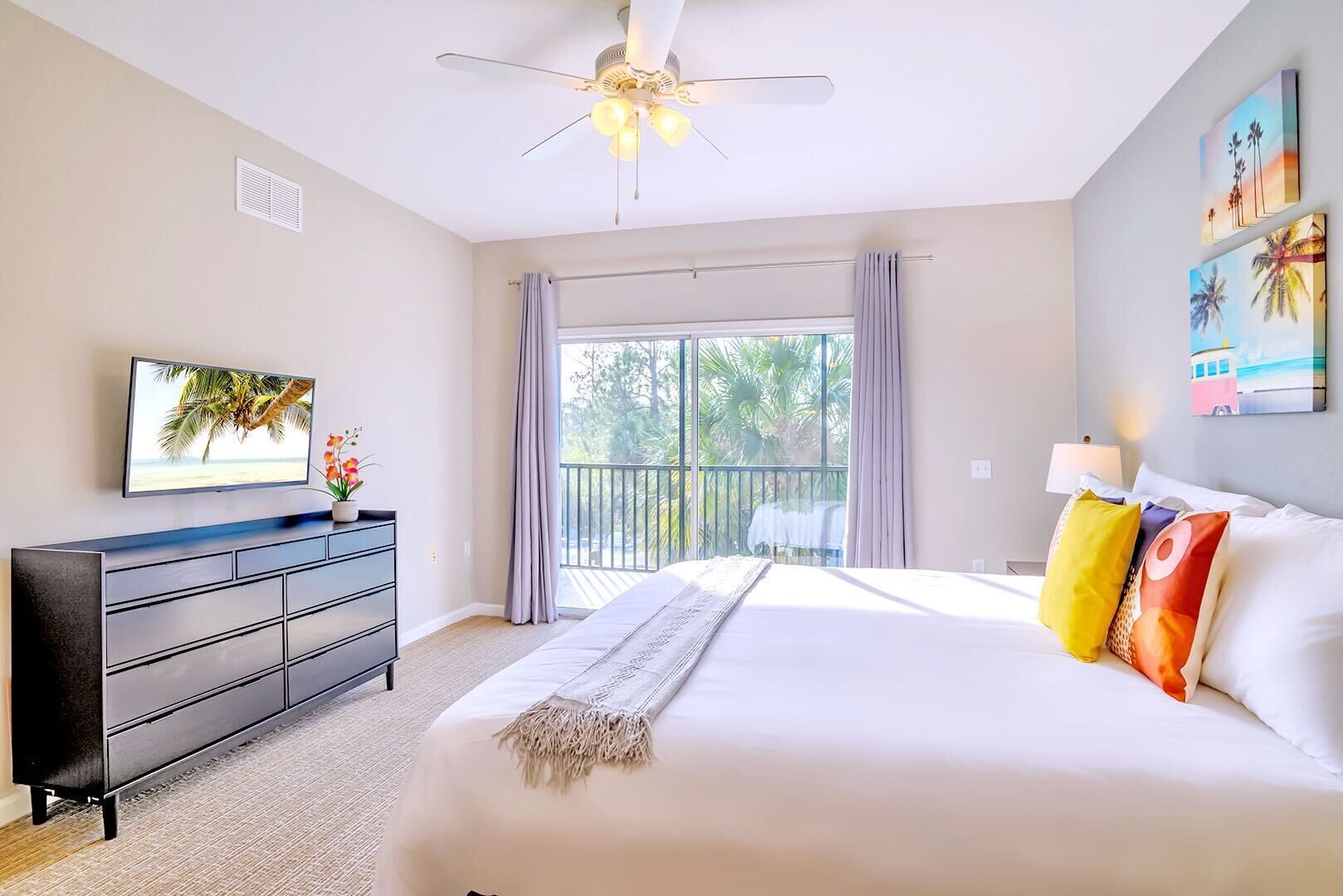 Une chambre d’hôtel comprenant un lit, une commode, une télévision et un balcon avec des rideaux.