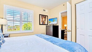 A bedroom with a bed, a dresser, a TV, and a window with blinds. - Condo 1BR Near Disney- Pool and Hot Tub! (Orlando)