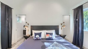 A modern bedroom with a large bed, two bedside tables with lamps, and a view of greenery through the window. - Stylish 3BR East Side Retreat w Patio & BBQ (Austin)