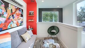 A modern living room with a red accent wall, a large abstract painting, a grey sofa, a black and white striped rug, and a round black chair. - Stylish 3BR East Side Retreat w Patio & BBQ (Austin)
