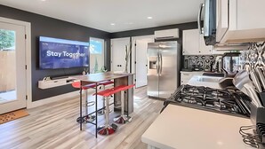 A modern kitchen with a TV displaying 'Stay Together', a stainless steel refrigerator, and a gas stove. - Stylish 3BR East Side Retreat w Patio & BBQ (Austin)