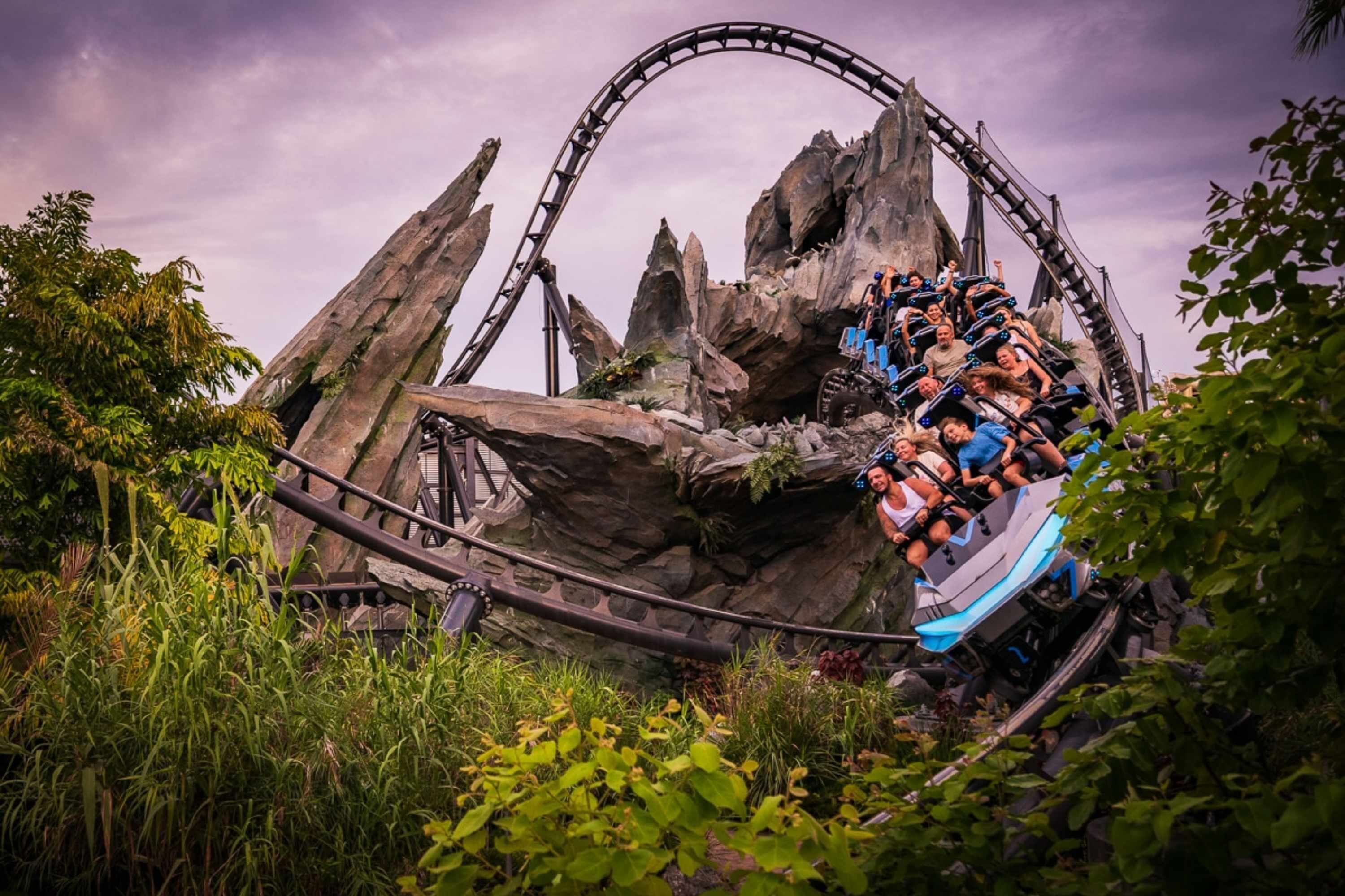 A roller coaster with a steep drop, surrounded by rocky terrain and greenery.