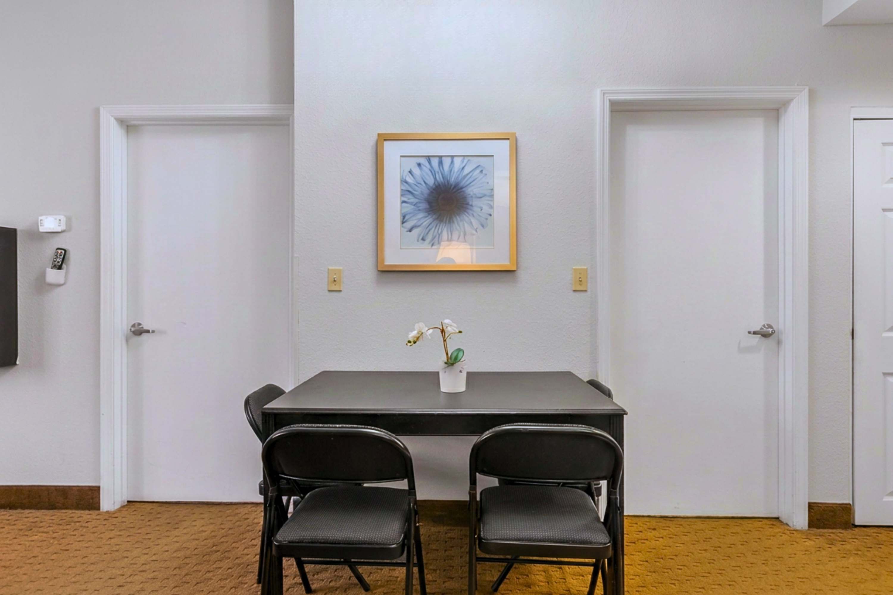 A conference room with a table, two chairs, a framed picture, and a small potted plant.