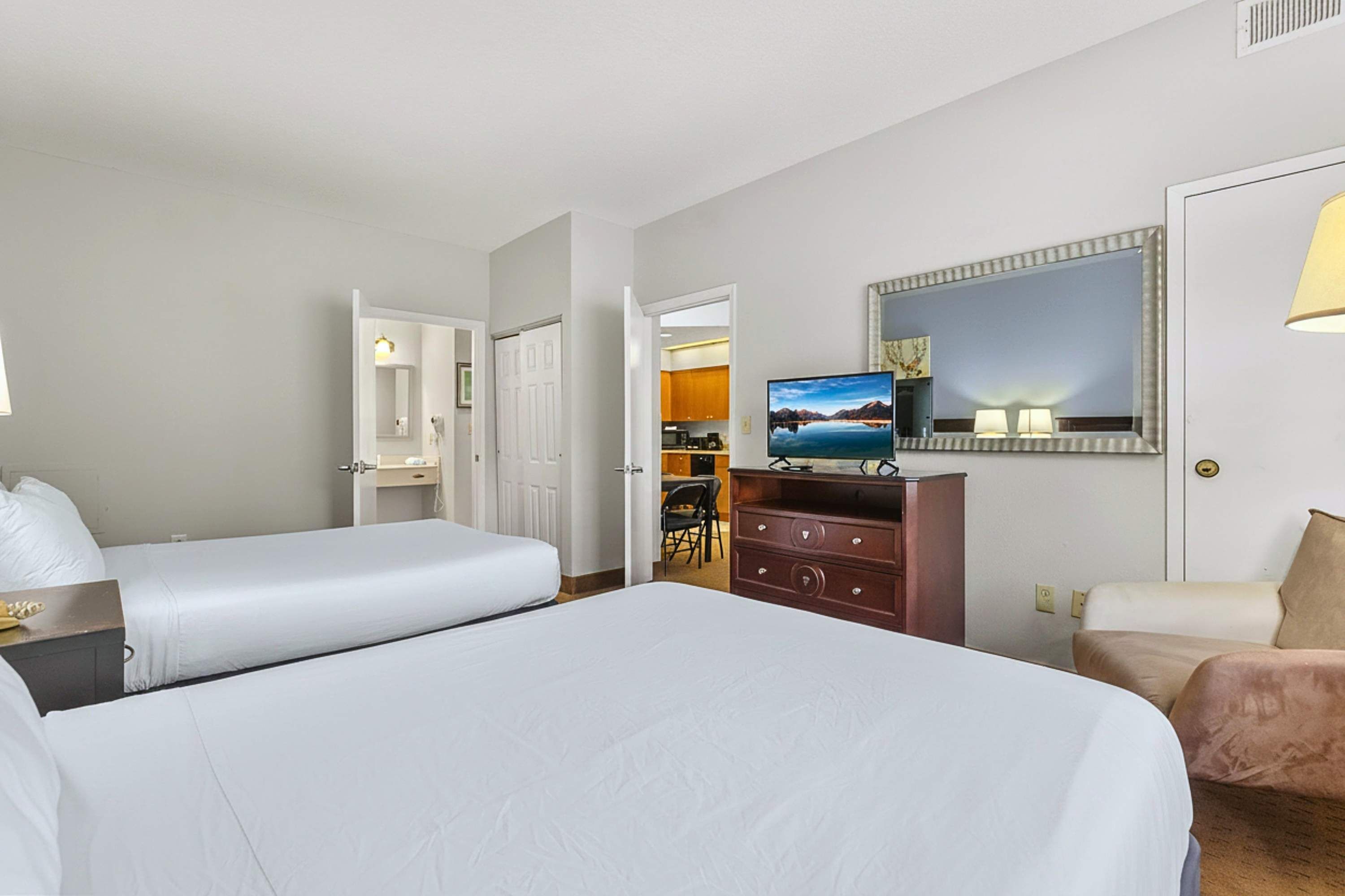Habitación de hotel con dos camas, televisor, espejo y escritorio.