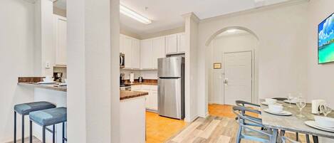 A modern kitchen with white cabinets, a stainless steel refrigerator, and a dining area with a table set for four.