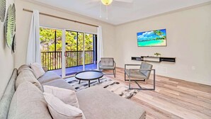 A spacious living room with a large sliding glass door leading to a balcony, a ceiling fan, a flat-screen TV, and a minimalist furniture arrangement. - Pet-friendly Resort Getaway With Patio and Pool (Winter Garden)