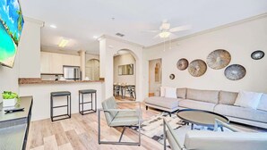 A modern living room with a sofa, coffee table, and a dining area with a TV. - Pet-friendly Resort Getaway With Patio and Pool (Winter Garden)