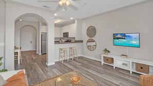 Una sala de estar moderna con televisor, asientos, cocina y ventilador de techo.