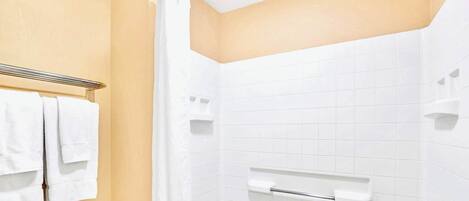A bathroom with a white bathtub, a towel rack with white towels, and a shower area with a white shower curtain.