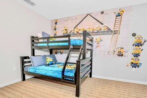 Un lit superposé avec une couverture et des oreillers bleus, une échelle et un mur décoré de personnages de « Moi, moche et méchant ».