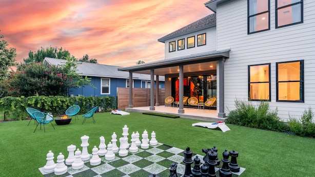 A modern house with a spacious backyard featuring a large chessboard, outdoor seating, and a well-maintained lawn. - Group Getaway With Chess Garden and Firepit (Austin)