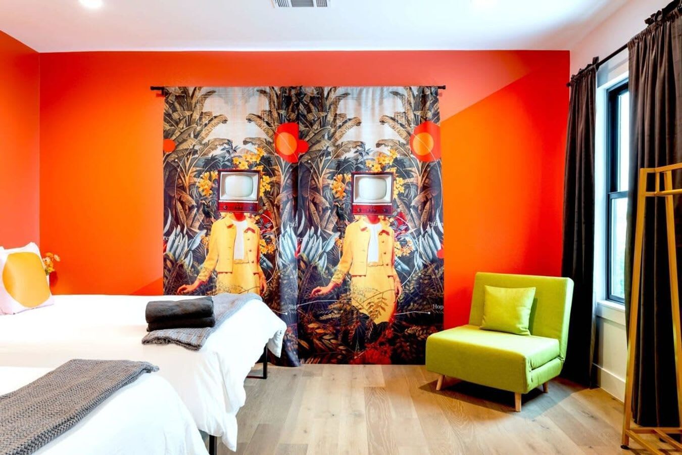 A hotel room with a large bed, a green armchair, and a vibrant red wall with a unique tapestry.