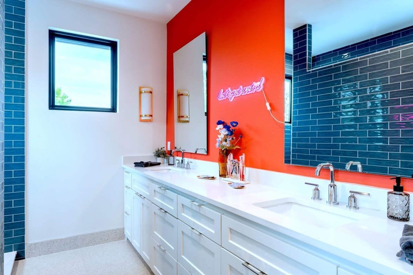 Ein modernes Badezimmer mit zwei Waschbecken, einem großen Spiegel und einer Neonreklame.