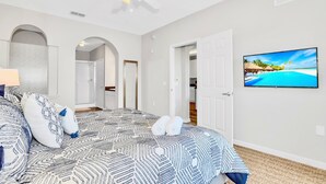 A bedroom with a patterned bedspread, a ceiling fan, a TV on the wall, and a view of a beach scene.