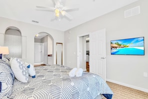 Quarto com colcha estampada, ventilador de teto, televisão na parede e vista para a praia.