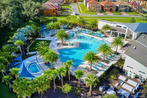 An aerial view of a resort with a large swimming pool surrounded by palm trees, a covered seating area, and a residential building in the background. - Upstay Wonderful Resort Home w Patio & Pool Sleeps 26 (Kissimmee)