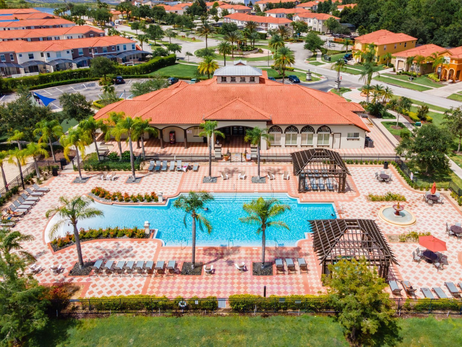 A resort with a central pool, multiple lounge areas, and a large building with a red roof.