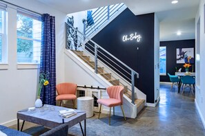 Un interior moderno con una escalera, una zona de comedor y una pared con un letrero de neón.