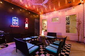 An outdoor seating area with wicker furniture, a checkered floor, a neon sign, and a fire pit. - Private Mini Golf and Covered Fireplace Lounge (Austin)