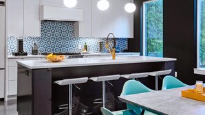 A modern kitchen with a central island, bar stools, and a window with a view of greenery. - Mini Golf & Fireplace - East Austin Group Retreat (Austin)