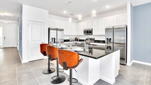 A modern kitchen with white cabinets, stainless steel appliances, and a central island with bar stools. - Upstay Luxury Resort Home w Private Pool & Hot Tub (Kissimmee)
