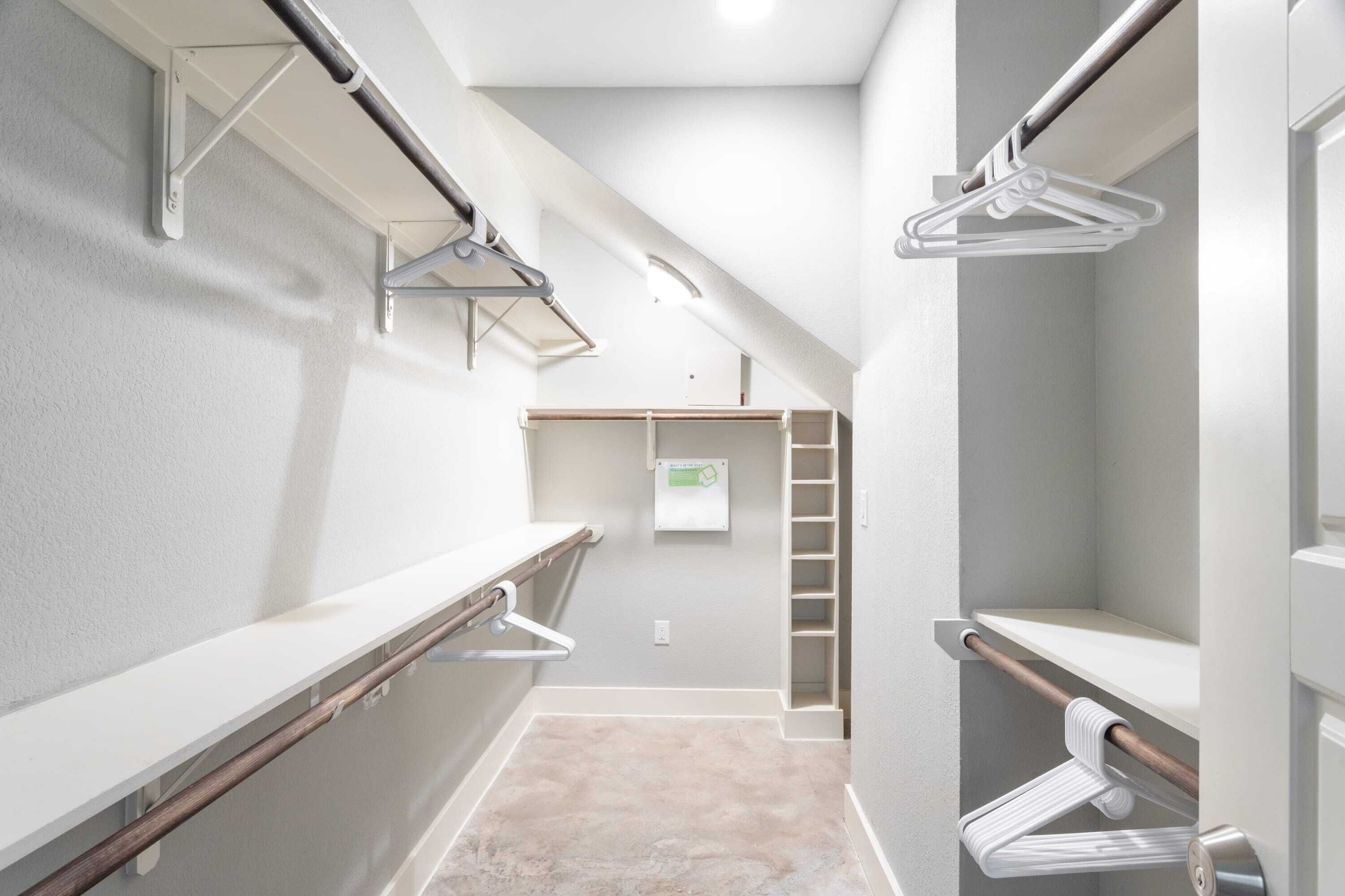 A narrow hallway with a white wall, a wooden bench, and a metal rack with hangers.