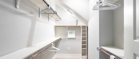 A narrow hallway with a white wall, a wooden bench, and a metal rack with hangers.