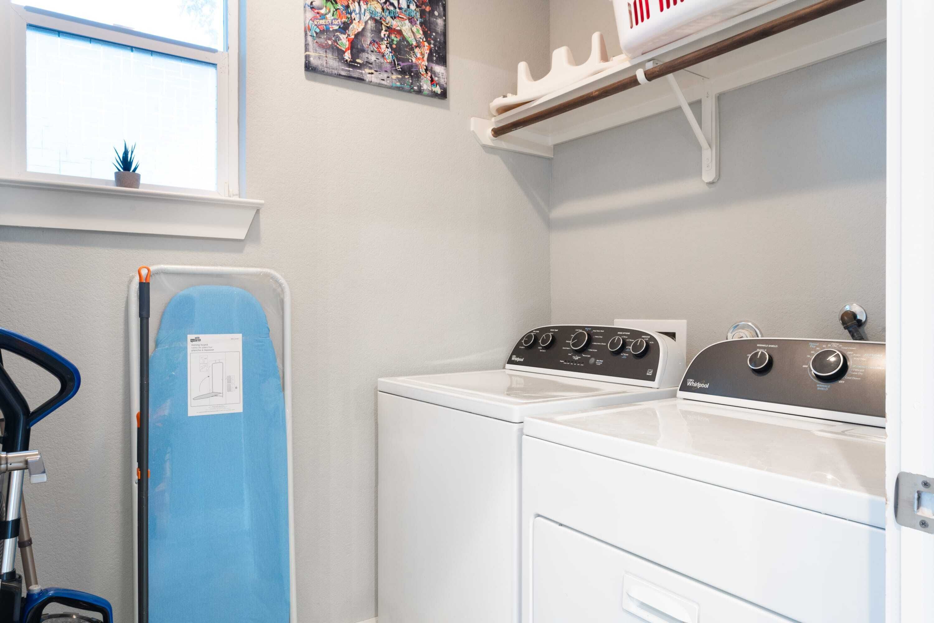Une buanderie équipée d’un lave-linge, d’un sèche-linge et d’une planche à repasser bleue.