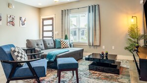 A modern living room with a grey sofa, blue armchair, and a coffee table. - Upstay Entertainment Hub w Games & Outdoor Firepit (Austin)