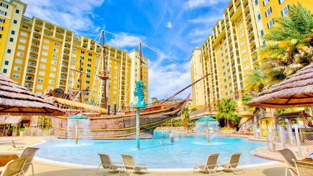 A hotel pool area with a ship-shaped water feature, lounge chairs, and high-rise buildings in the background. - Buena Vista Resort Condo w/ Pool & Private Patio (Orlando)