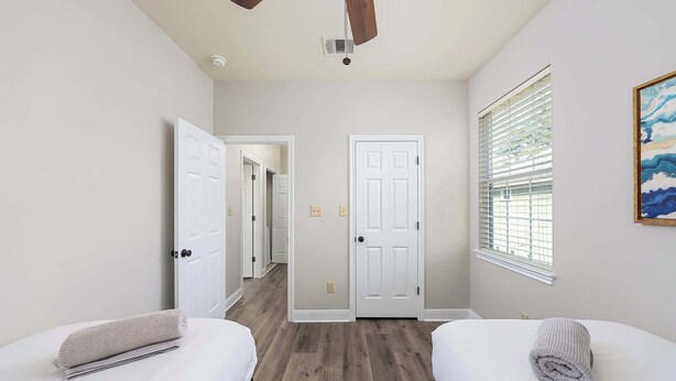Une chambre avec deux lits, un ventilateur de plafond, une porte et une fenêtre avec des stores.