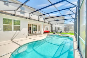 Piscina coberta com teto de vidro, ao lado de uma casa com terraço e área de estar externa.