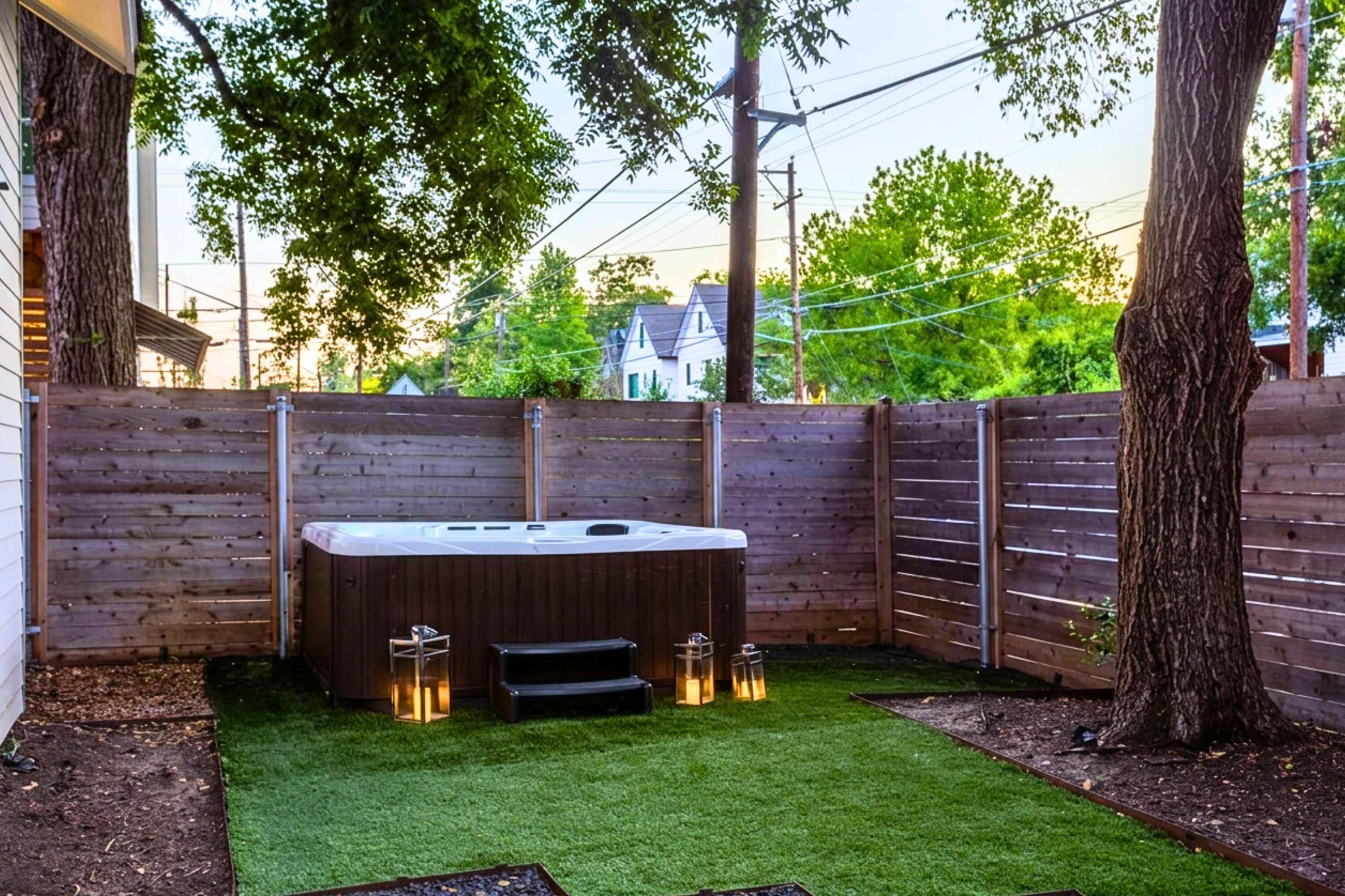 A hot tub in a backyard with artificial grass, wooden fence, and trees.