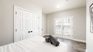 Ein Schlafzimmer mit einem Bett, zwei weißen Türen und Blick durch eine Glastür.