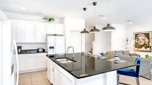 Une cuisine moderne avec des armoires blanches, un comptoir noir et un îlot central doté d’un évier. Trois luminaires suspendus sont placés au-dessus de l’îlot.