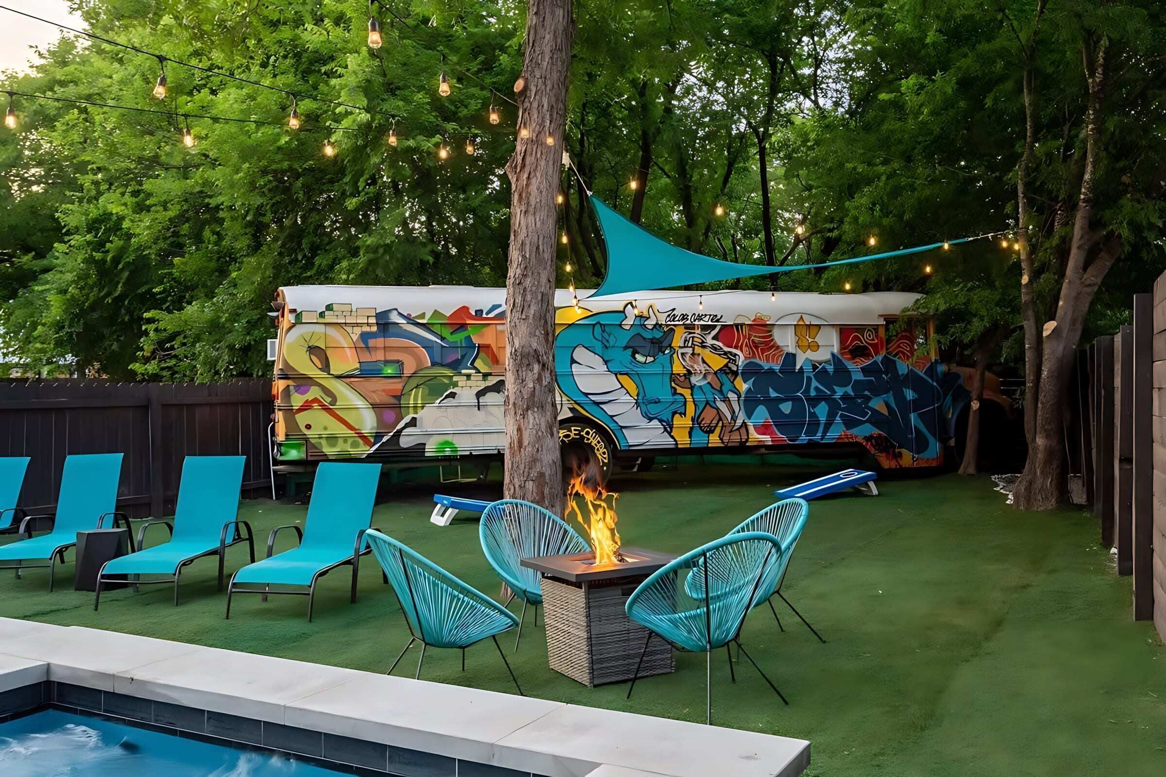 A backyard with a pool, blue chairs, a fire pit, and a colorful mural on a wall.