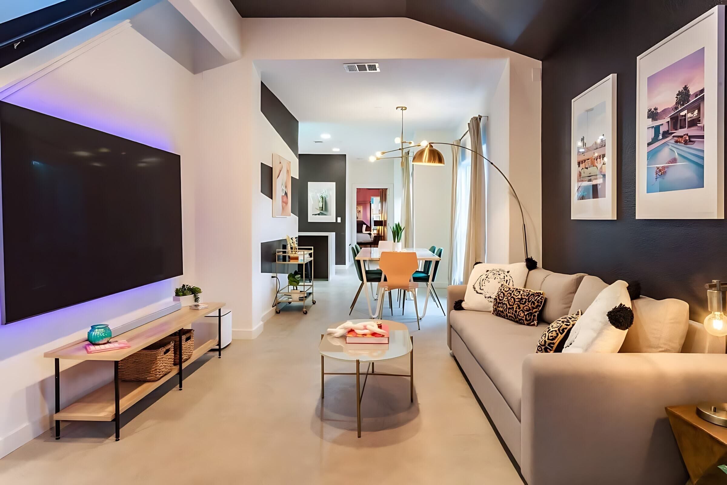 Ein modernes Wohnzimmer mit Flachbildfernseher, einer Couch, einem Couchtisch und einem Essbereich im Hintergrund.