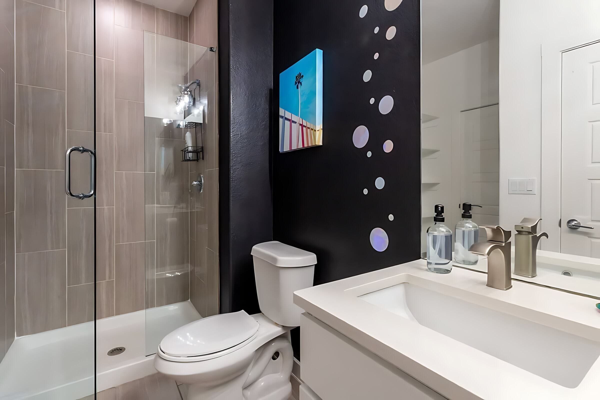 A modern bathroom with a glass-enclosed shower, a white toilet, and a white sink with a mirror.