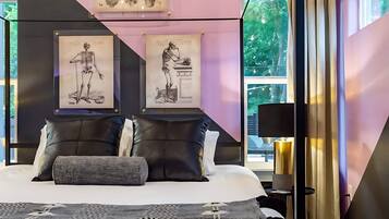 A modern bedroom with a bed, pillows, a nightstand, a lamp, and framed anatomical illustrations on the wall.