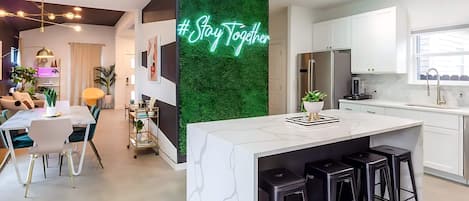 A modern kitchen with white cabinets, a central island with bar stools, and a neon sign saying "#StayTogether".