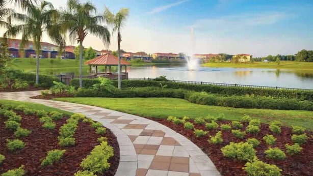 Un jardin aménagé avec un chemin pavé, des palmiers et un bassin d’eau orné d’une fontaine.