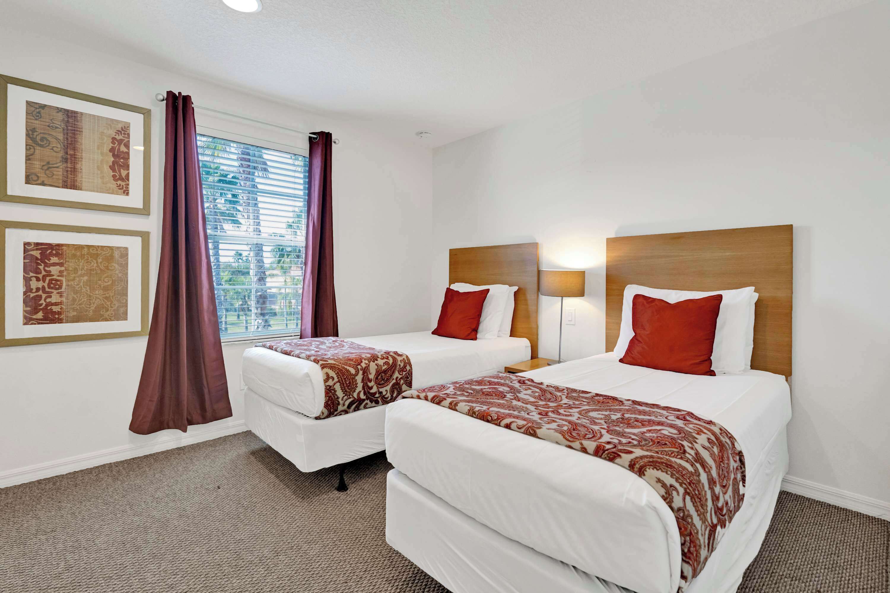 A hotel room with two beds, a window with curtains, and framed artwork on the wall.