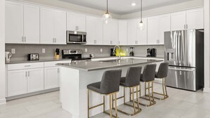 A modern kitchen with white cabinets, stainless steel appliances, and a central island with bar stools. - Upstay: Poolside Mansion w/ Themed Arcade & Cinema (Four Corners)